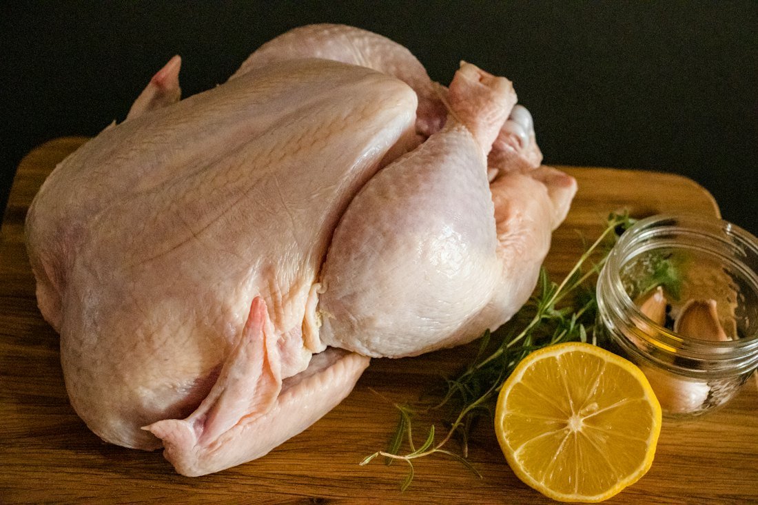 Whole raw chicken on a cutting board with lemon and herbs
